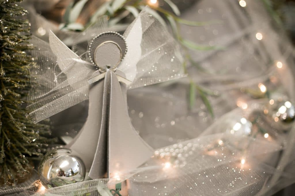 Angel Ornament with silver and white holiday lights and ornaments in the background