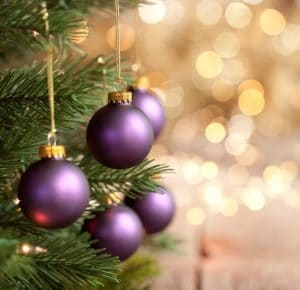 Christmas tree with purple baubles and gold lights against a bokeh background