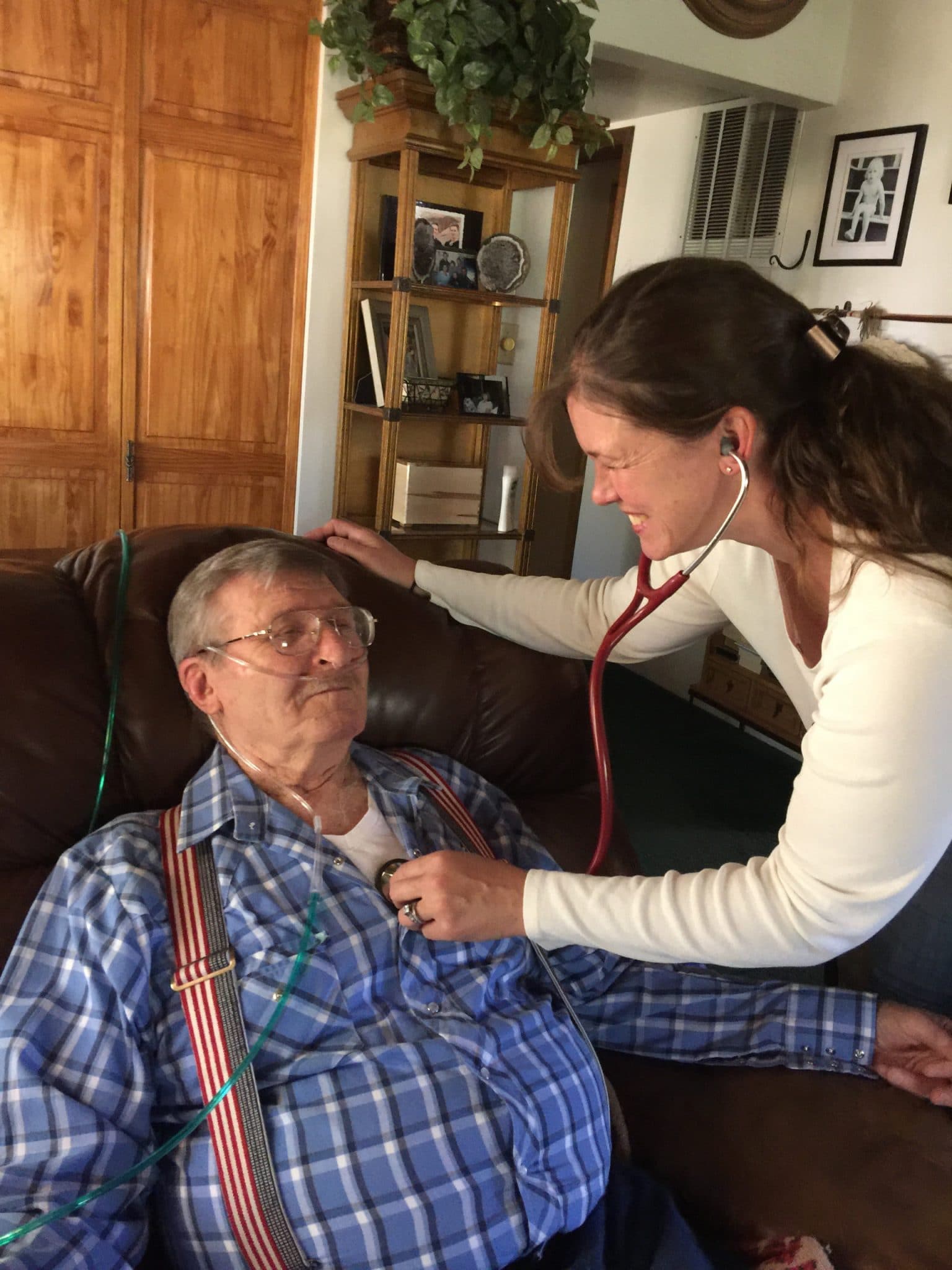 Female Mount Evans' RN with her oxygen dependent patient while she auscultates his lung sounds. Both individuals are smiling and having a good moment.