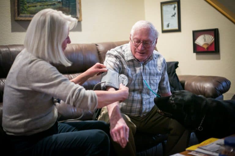 Palliative care patient having his blood pressure taken in his living room by Mount Evans employee