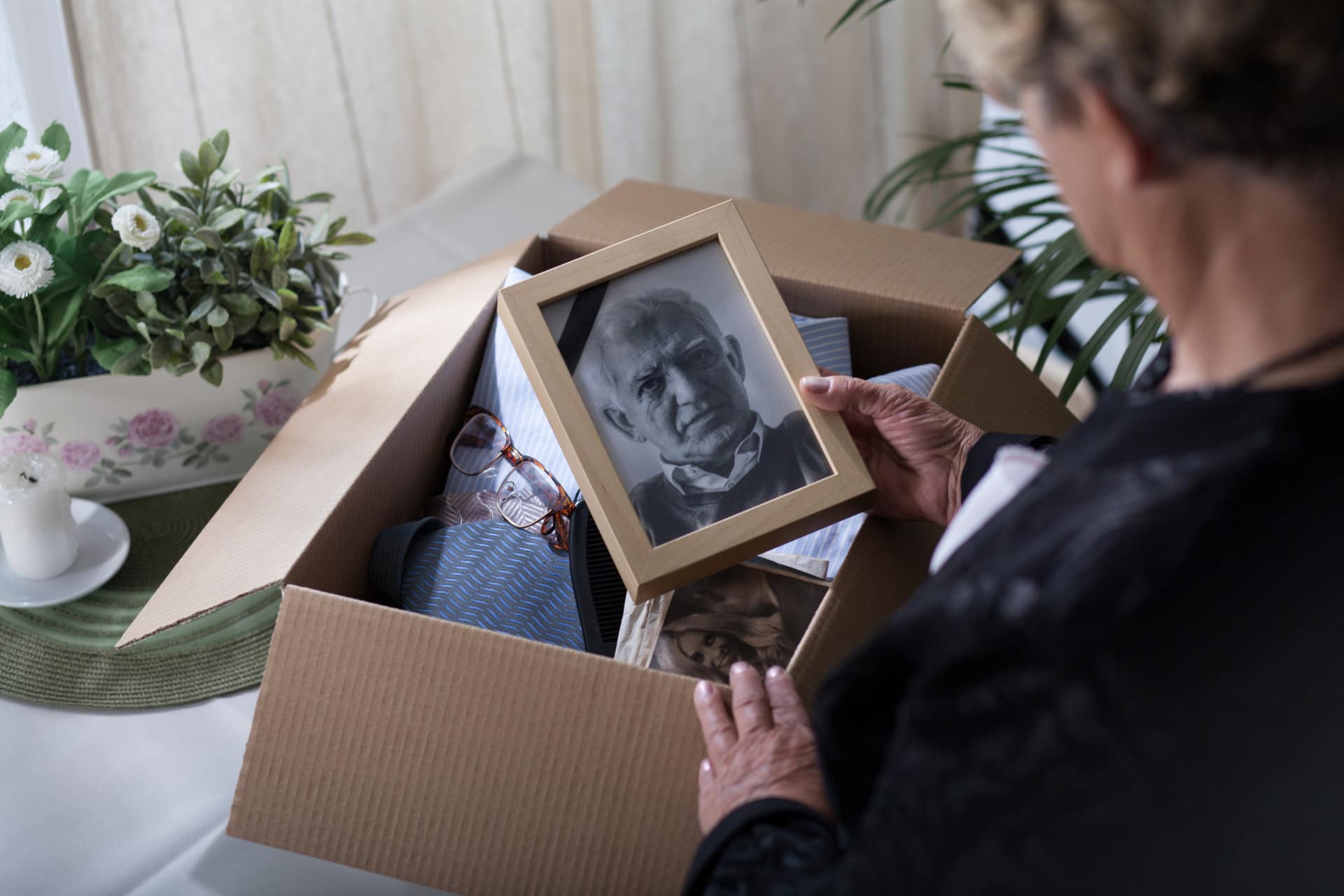 Woman is packing up belongings and memories of her deceased husband while looking a portrait photo of him