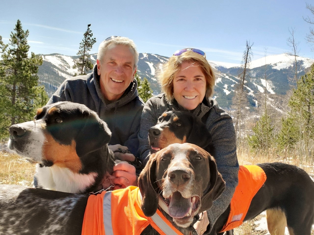 Mount Evans CEO, Keri Jaeger with husband and three dogs in mountains with ski hill in distance