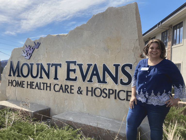 Lauren Guzman, Clinical Supervisor, LPN in front of the Mount Evans Home Health Care & Hospice sign
