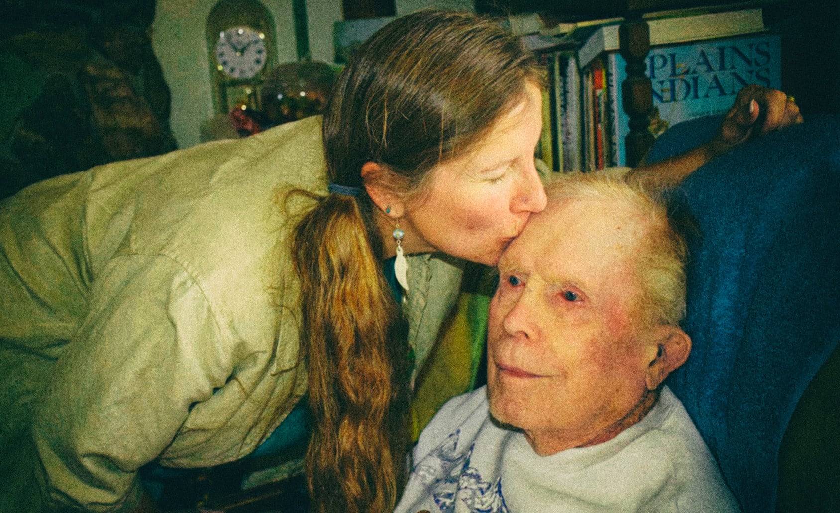About Us Page Image Header showing a female care giver placing a kiss on an elderly patient's forehead